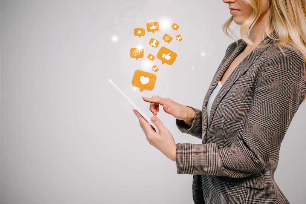 обрізаний вид на бізнес-леді в костюмі, який торкається цифрового планшета з мультимедійними іконками ізольовані на сірому
 - Фото, зображення