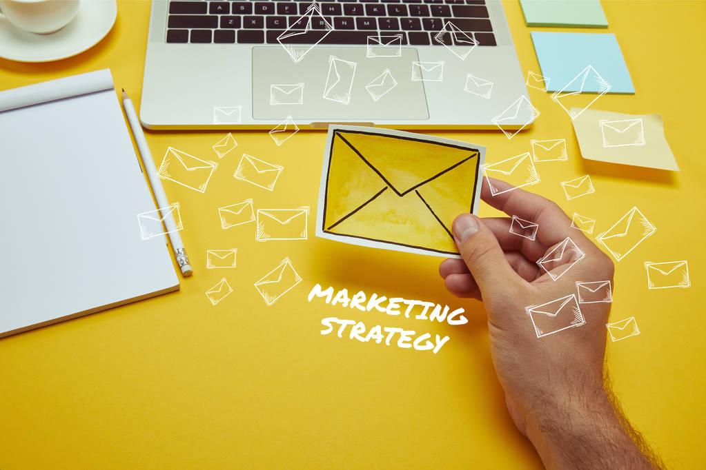 imagem cortada do homem segurando envelope sinal perto do laptop com "estratégia de marketing" lettering e ícones de e-mail
 - Foto, Imagem