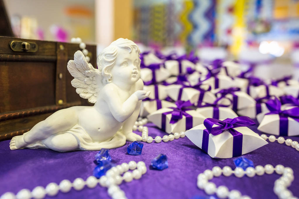 Keramikengel auf dem Tisch mit violettem Tischtuch und kleinen Geschenken für die Gäste des Brautpaares - Foto, Bild