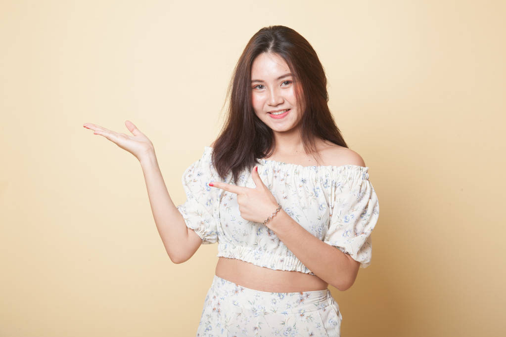 Beautiful young Asian woman point to palm hand on beige background - Photo, Image