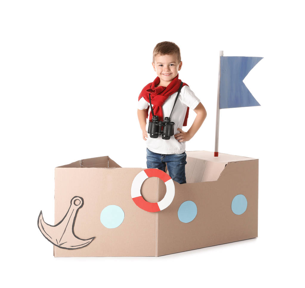 Χαριτωμένο μικρό αγόρι παίζει με χαρτόνι πλοίο σε λευκό φόντο - Φωτογραφία, εικόνα