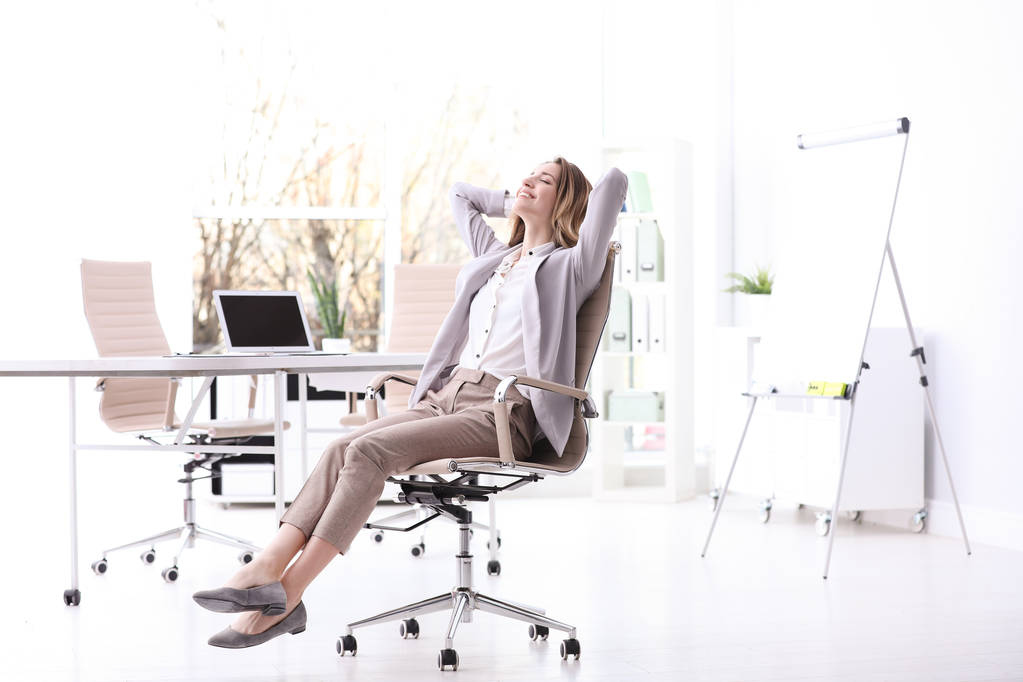 Nuori nainen istuu nojatuolissa työpaikalla
 - Valokuva, kuva