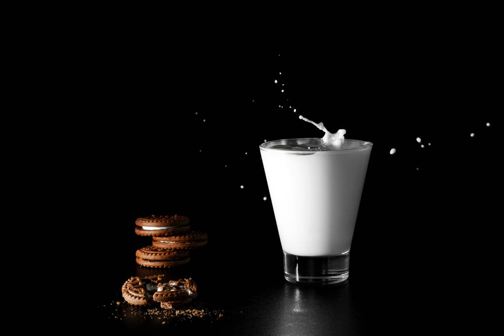 Splash in glass of milk and chocolate cookies on black background. - Photo, Image
