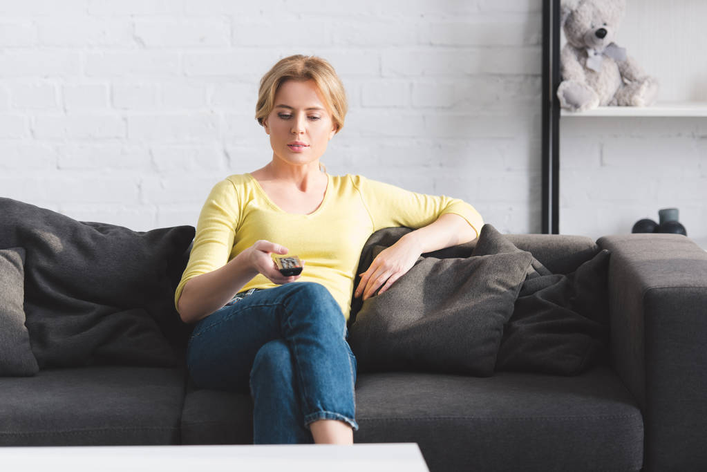 atractiva mujer sentada en el sofá y el uso de mando a distancia
 - Foto, Imagen