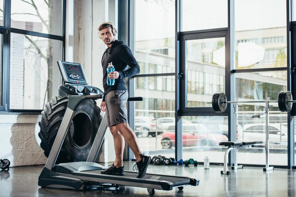 yakışıklı sporcu treadmill egzersiz ve spor şişe su içinde jimnastik salonu tutan hoodie  - Fotoğraf, Görsel