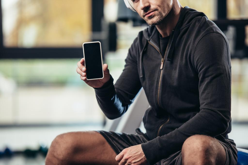 Ausgeschnittenes Bild eines Sportlers zeigt Smartphone mit leerem Bildschirm im Fitnessstudio  - Foto, Bild