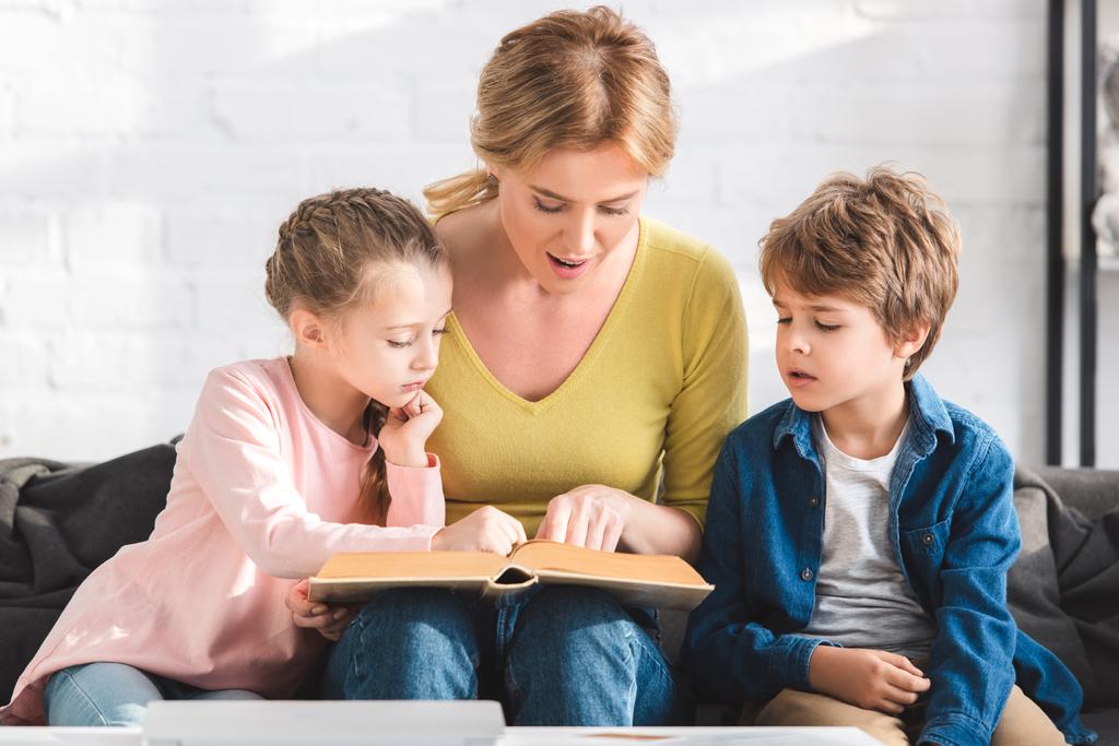 Gelukkig moeder met schattige kleine kinderen zitten samen op de Bank en readng boek - Foto, afbeelding