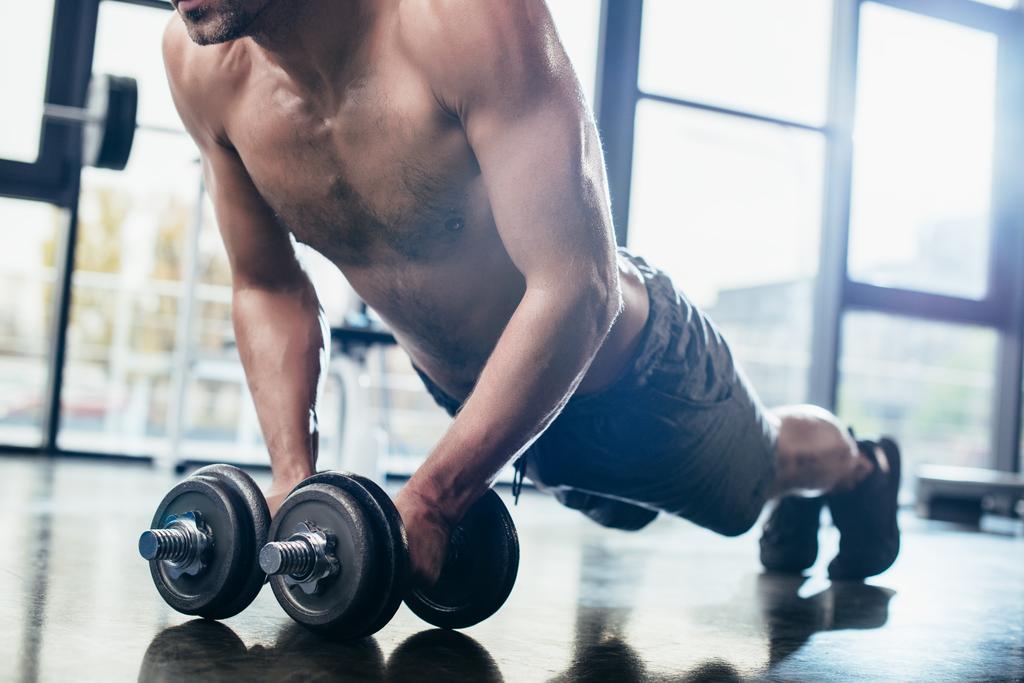 cropped image of shirtless sportsman doing plank on dumbbells in gym  - Photo, Image