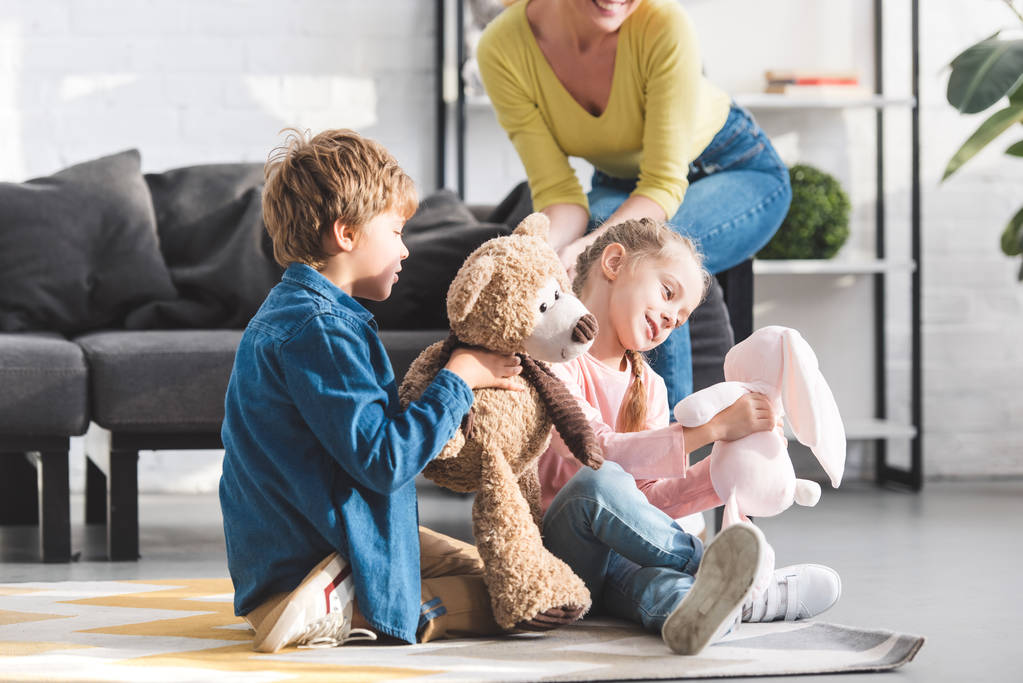 Schnappschuss einer glücklichen Mutter, die auf der Couch sitzt und niedlichen kleinen Kindern, die zu Hause mit Spielzeug spielen - Foto, Bild