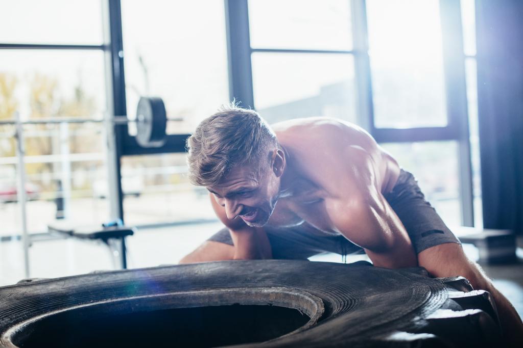 handsome shirtless sportsman lifting heavy tire in gym  - Photo, Image