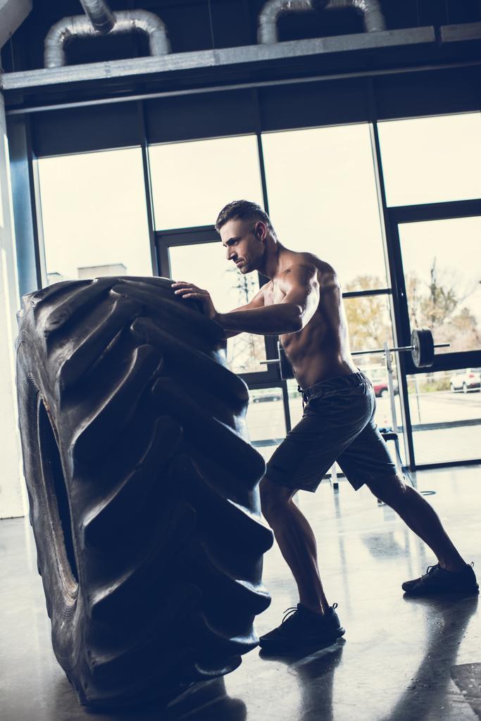 vista lateral del guapo deportista sin camisa levantando neumáticos en el gimnasio
  - Foto, imagen