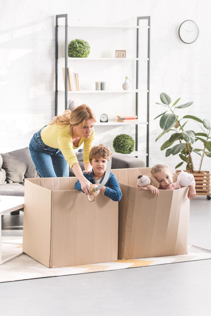 emotional mother looking at naughty children playing in cardboard boxes - Photo, Image