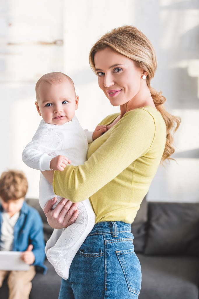 schöne glückliche Mutter hält entzückendes Kleinkind in der Hand und lächelt in die Kamera - Foto, Bild