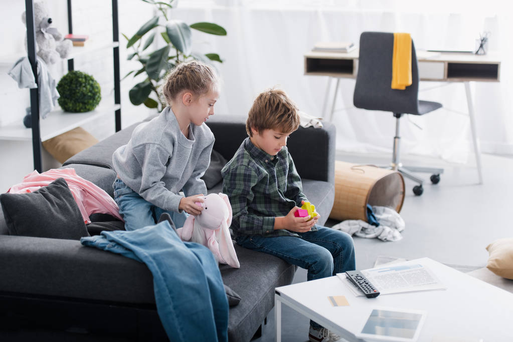 visão de alto ângulo de irmãos sentados no sofá e brincando com brinquedos em casa
 - Foto, Imagem