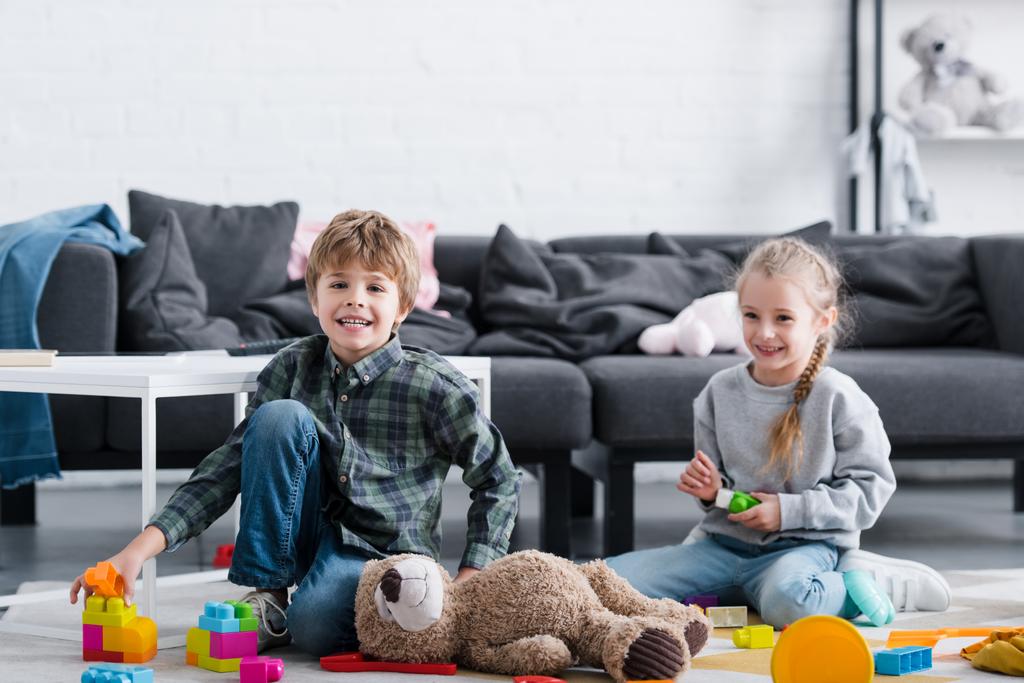 schattig gelukkige kinderen zittend op de vloer en spelen met speelgoed thuis - Foto, afbeelding