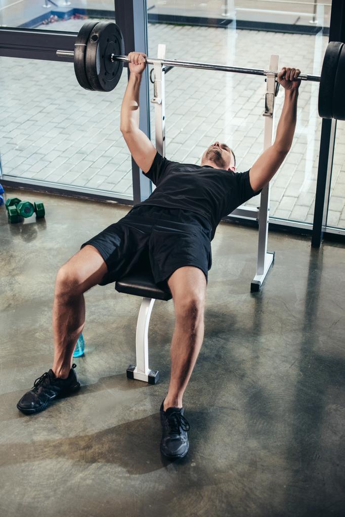 pohledný sportovec zvedání činka s váhami vleže na lavici v tělocvičně  - Fotografie, Obrázek