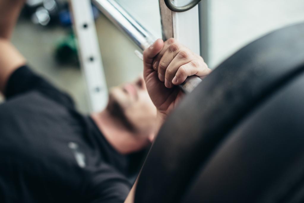 selektiver Fokus des Sportlers beim Hantelheben mit Gewichten im Liegen auf der Bank im Fitnessstudio  - Foto, Bild