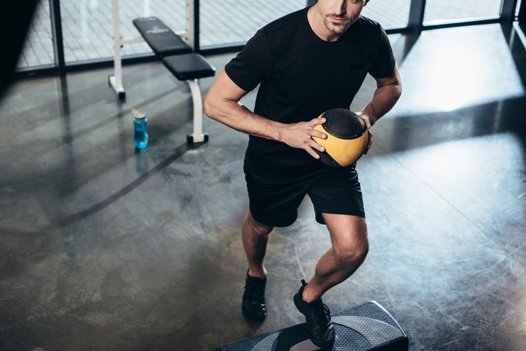 обрезанный имидж спортсмена тренирующегося на ступенчатой площадке с медицинским мячом в тренажерном зале
 - Фото, изображение