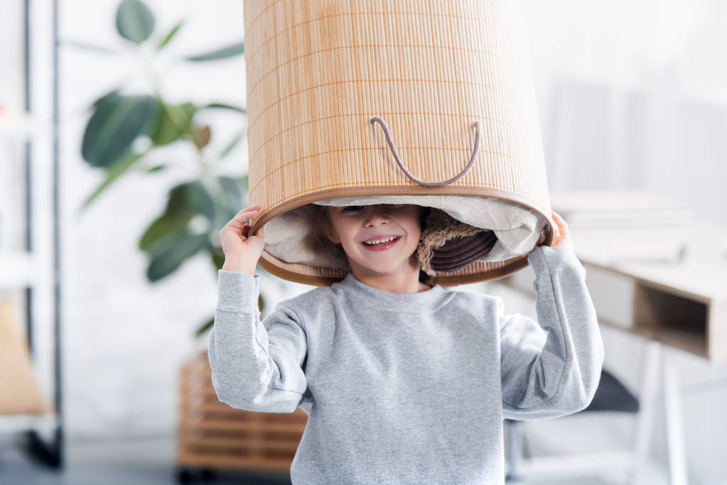 милий щасливий дитина грає з кошиком для білизни на голові
 - Фото, зображення