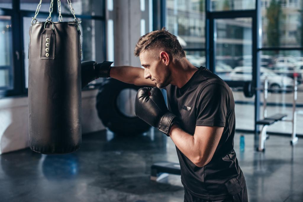 vista lateral del guapo entrenamiento de boxeador muscular con saco de boxeo en el gimnasio
 - Foto, imagen