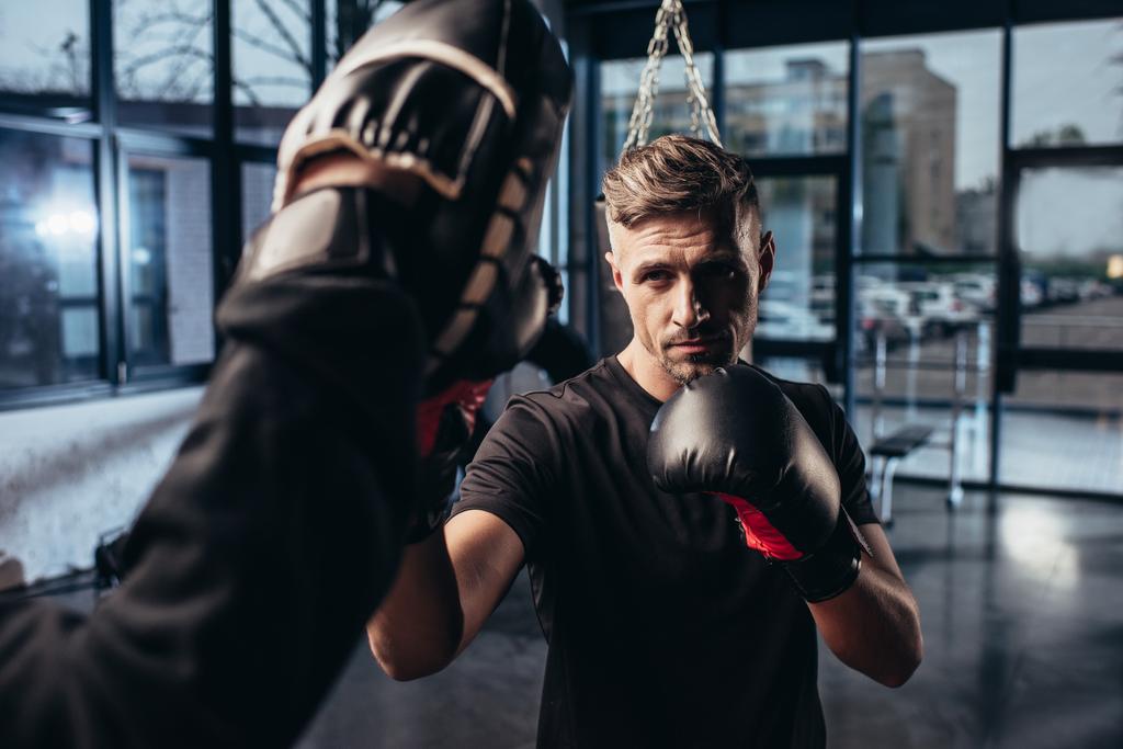 selective focus of handsome boxer exercising with trainer in gym - Photo, Image