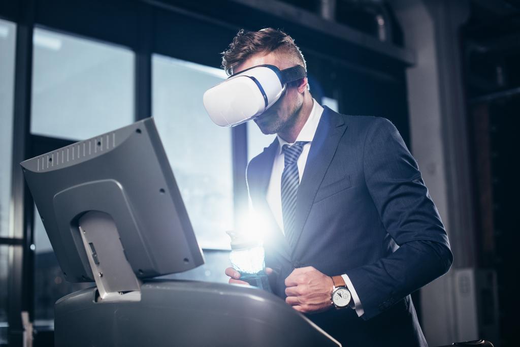 vista de bajo ángulo del hombre de negocios en traje y auriculares de realidad virtual haciendo ejercicio en la cinta de correr en el gimnasio
 - Foto, imagen