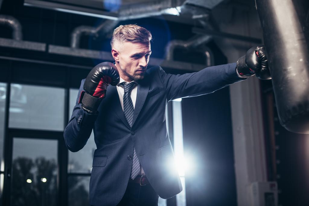 pohledný podnikatel v obleku boxu s boxovací pytel v tělocvičně - Fotografie, Obrázek
