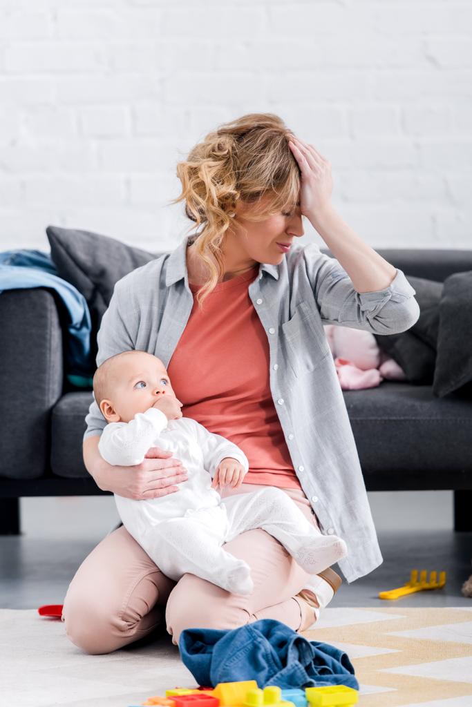 kimerült anya csecsemőgondozási gazdaság, és ül, kezével a homlokát a földre - Fotó, kép