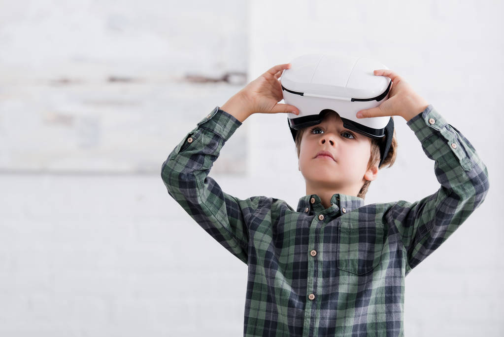 очаровательный мальчик, использующий гарнитуру виртуальной реальности и глядя в сторону дома
 - Фото, изображение
