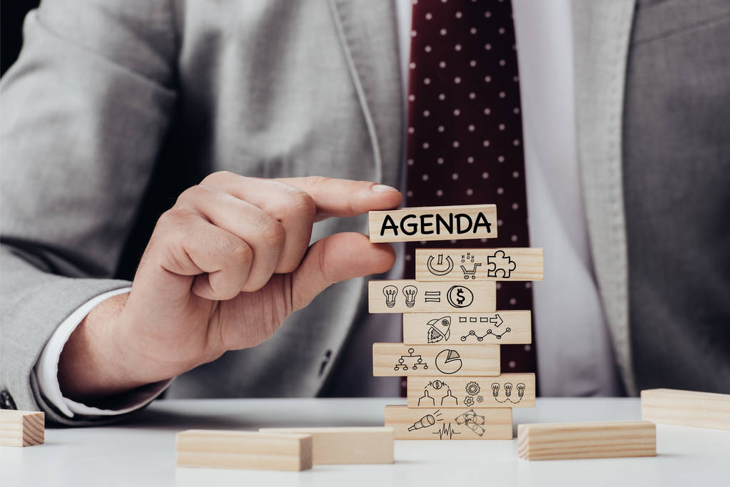 cropped view of man holding brick with word 'agenda' over wooden blocks with icons - Photo, Image