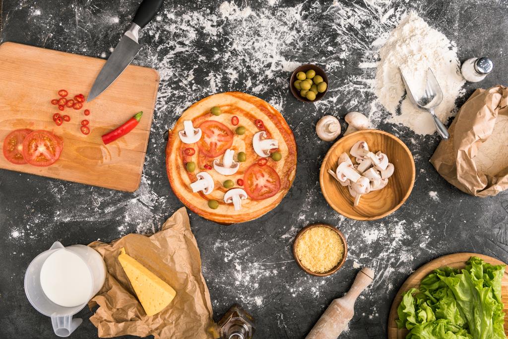 ylhäältä näkymä kypsentämättömät pizza ja ainesosat harmaalla pohjalla jauhoja
  - Valokuva, kuva
