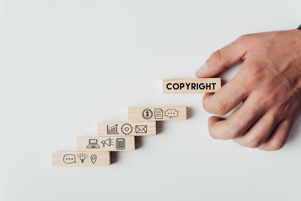 oříznutý pohled člověka drží dřevěný blok s slovo "autorských práv" na vrcholu dřevěné cihly s ikonami izolované na bílém - Fotografie, Obrázek