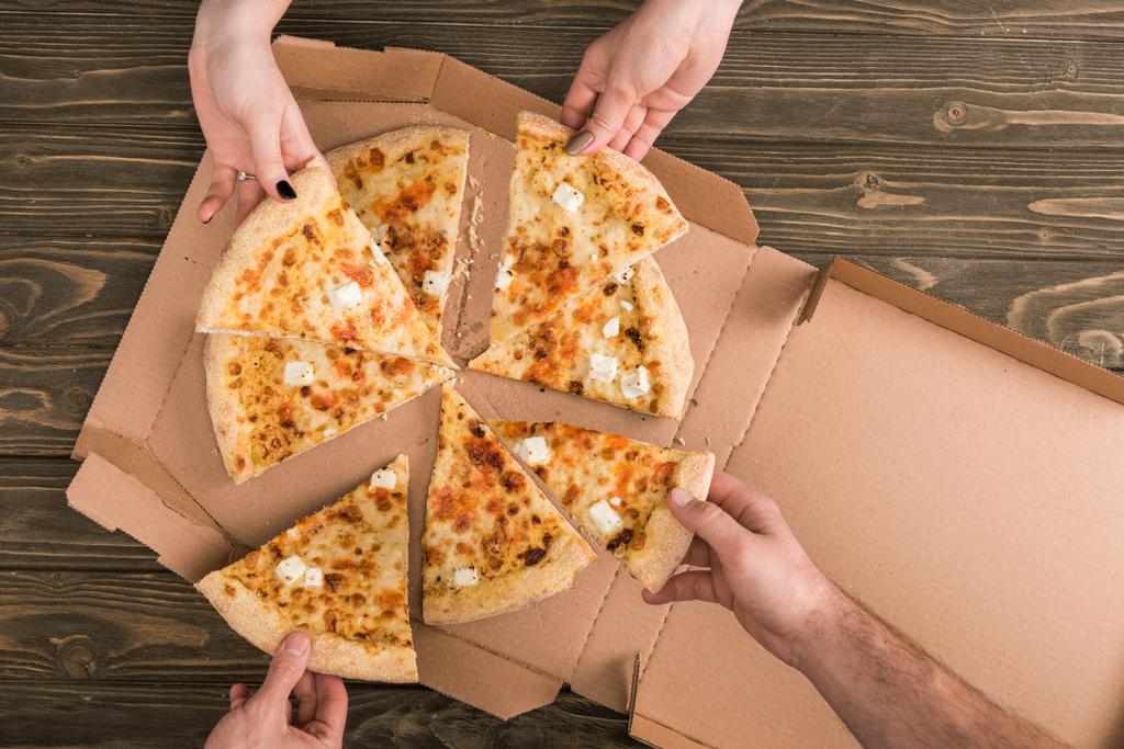обрізаний вид друзів, які їдять сирну піцу на дерев'яному столі
 - Фото, зображення