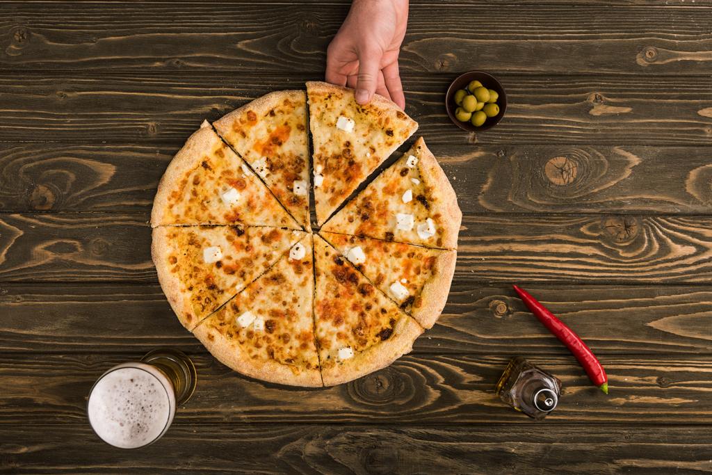 vista parcial del hombre comiendo pizza de queso sobre una mesa de madera con cerveza y aceitunas
 - Foto, imagen