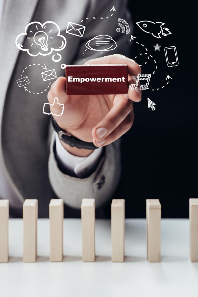partial view of man holding red brick with word 'empowerment' isolated on black, icons on foreground - Photo, Image