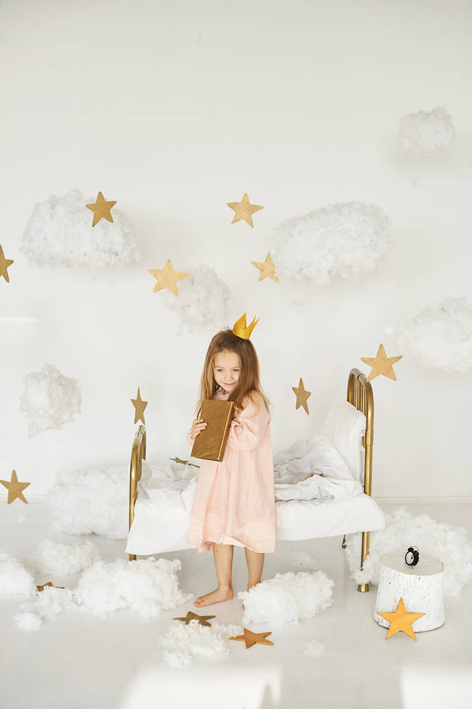 Pequena princesa com uma varinha mágica na cama em uma nuvem em um fundo branco
 - Foto, Imagem