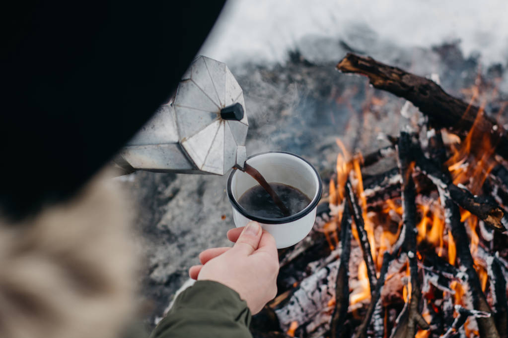 A mulher viajante um senta-se perto do fogo de acampamento um no tempo de inverno e derrama-se o café quente. Conceito aventura férias ativas ao ar livre. Camping de inverno
 - Foto, Imagem