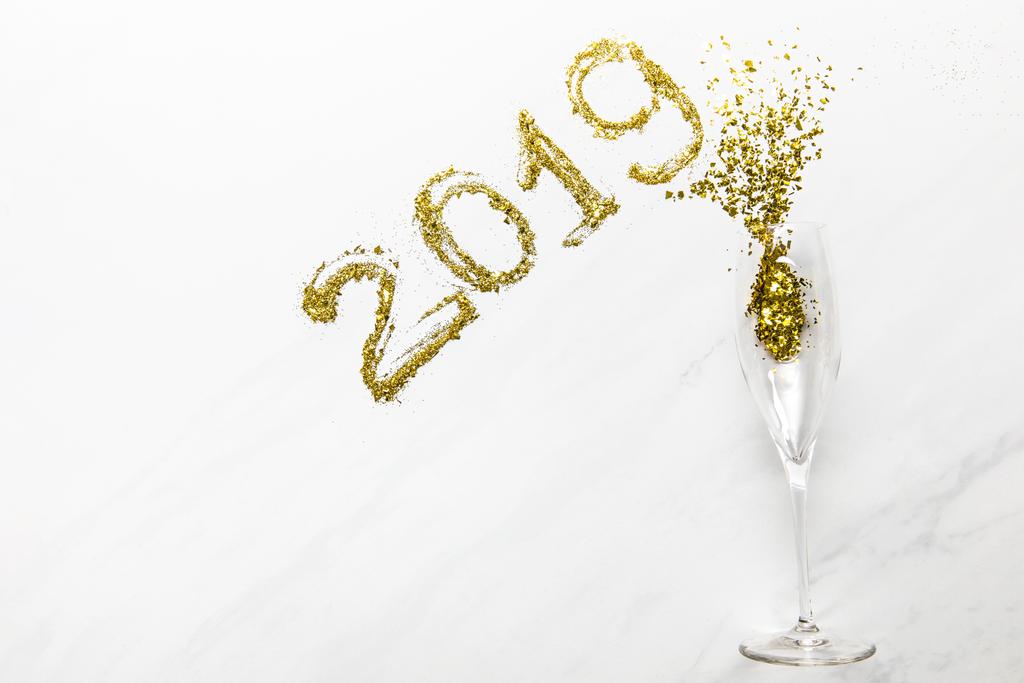 2019 nummers en champagne glas met gouden confetti op witte achtergrond - Foto, afbeelding