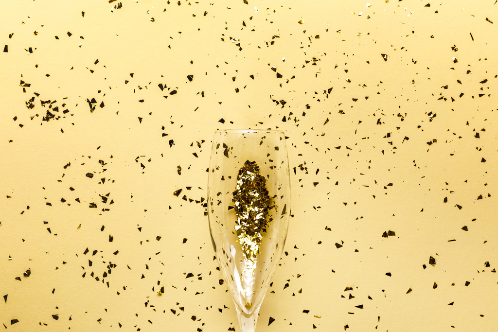 Champagne glas en feestelijke gouden confetti op beige achtergrond   - Foto, afbeelding