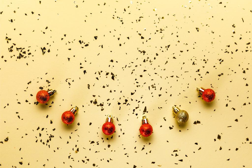 top view of red and golden christmas baubles and shiny confetti on beige background - Photo, Image