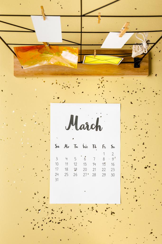 Ansicht des Märzkalenders mit goldenem Konfetti und Karten mit Wäscheklammern auf beige - Foto, Bild