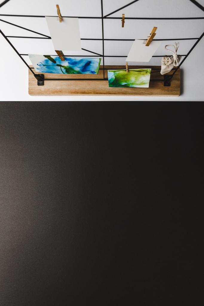 bovenaanzicht van prachtige abstracte schilderijen en blanco kaarten hangen van wasknijpers, zwarte achtergrond  - Foto, afbeelding