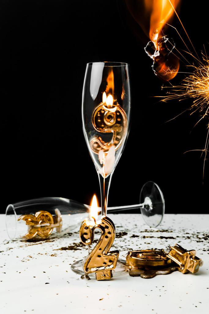 Nahaufnahme von Sektgläsern mit Kerze, Wunderkerze und goldenen Zahlen 2019 auf Schwarz  - Foto, Bild