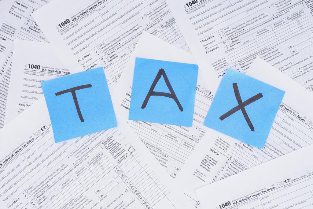 vista superior de la palabra 'tax' hecha de tarjetas azules con documentos en segundo plano
  - Foto, Imagen