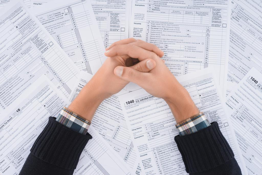 abgeschnittene Ansicht eines Mannes mit gefalteten Händen auf Hintergrund mit Steuerformularen - Foto, Bild