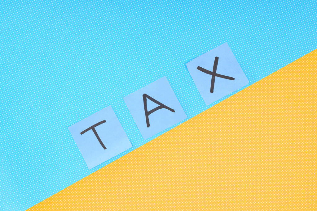 bovenaanzicht van het woord "belasting" gemaakt van kaarten op blauwe en gele achtergrond - Foto, afbeelding