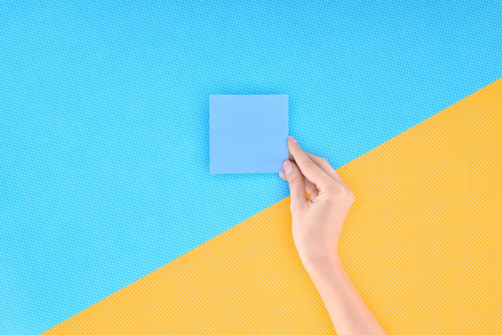 bijgesneden beeld van vrouw met lege blauwe kaart op blauwe en gele achtergrond - Foto, afbeelding