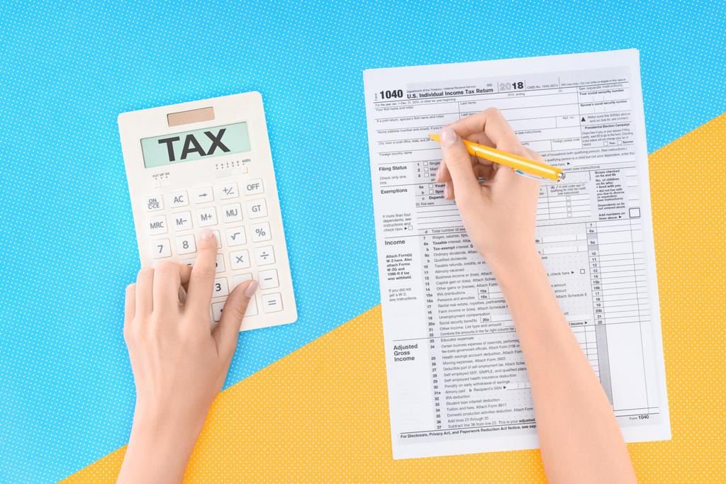 女性言葉「税」で電卓を使用して、青と黄色の背景の税務フォーム充填のトリミング ビュー - 写真・画像