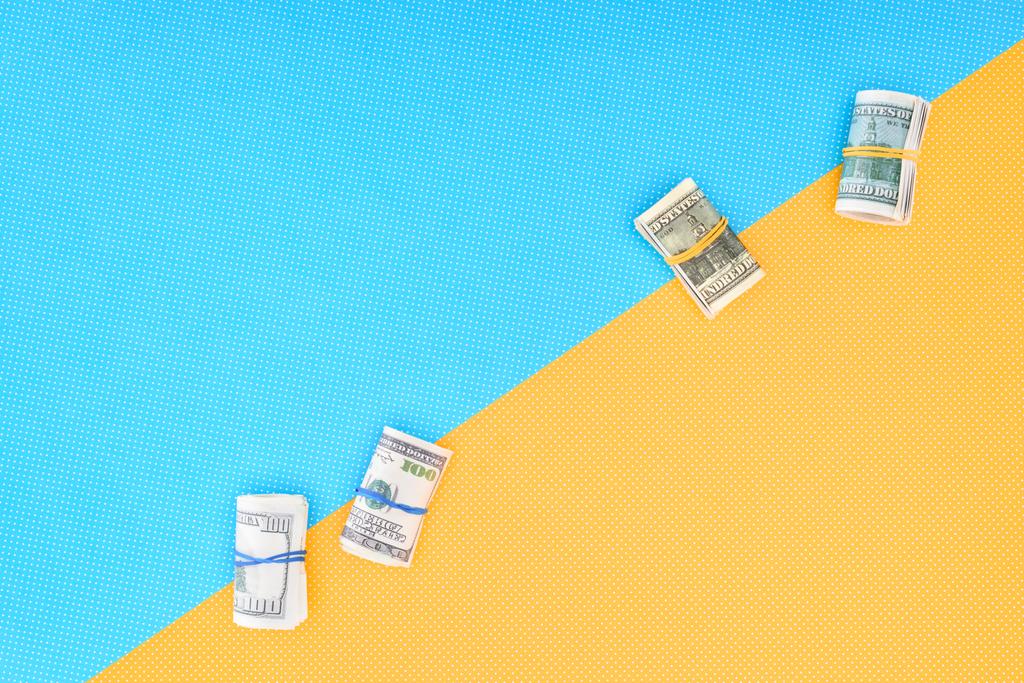 top view of money rolls on blue and yellow background with copy space - Photo, Image