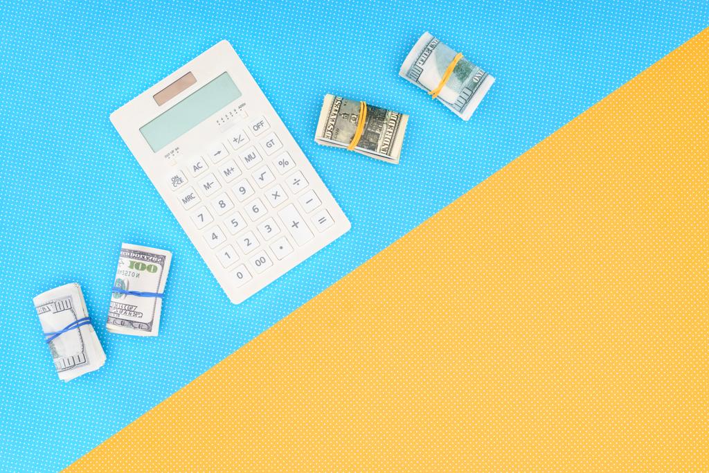 vista dall'alto della calcolatrice e rotoli di denaro su sfondo blu e giallo
 - Foto, immagini